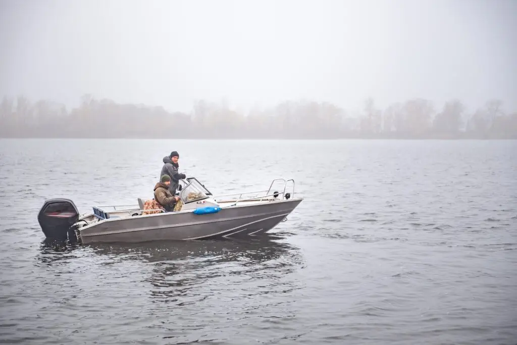 Anglers running a fishing boat on a lake in autumn